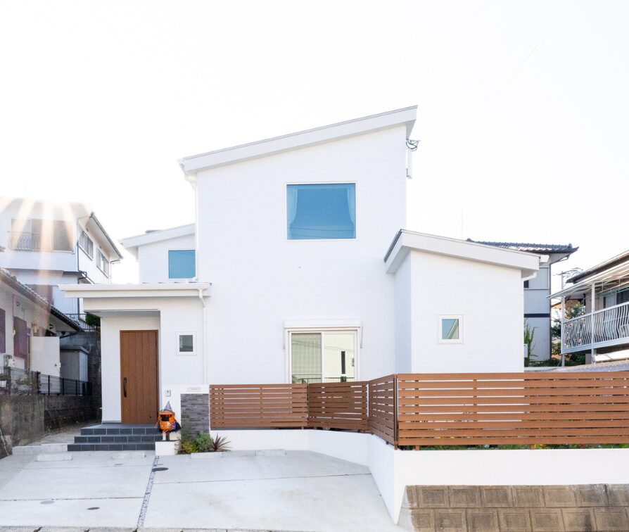 青空に映える白い外壁と木製フェンスが印象的な、光あふれる二階建て住宅の外観