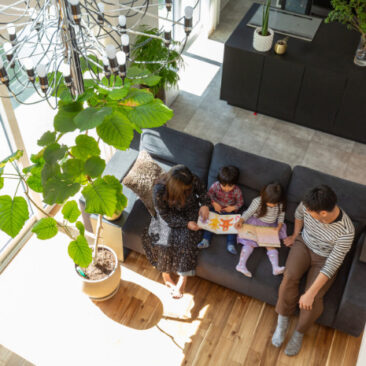 吹抜けリビングのソファで家族が並んで絵本を楽しむ、明るく穏やかな団らんの時間