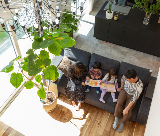 吹抜けリビングのソファで家族が並んで絵本を楽しむ、明るく穏やかな団らんの時間