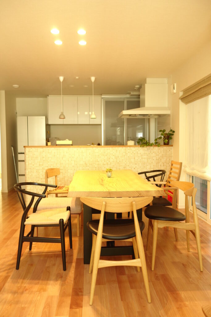 無垢材のダイニングテーブルと椅子を中心に、対面キッチンが続く明るいLDK空間