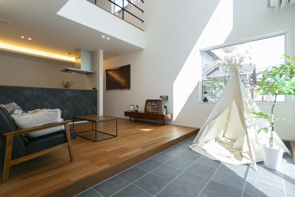 大きな窓から光が差し込む、開放的な吹き抜けのあるリビング。土間スペースに設置されたティピーテントと、アクセントとなるパキラの観葉植物。