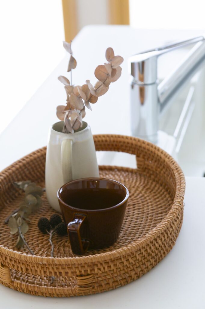 ラタンのトレーに載せられたコーヒーカップと、花瓶に生けられたユーカリ・ポポラスのドライフラワー。おうち時間を彩るナチュラルな雑貨コーディネート。