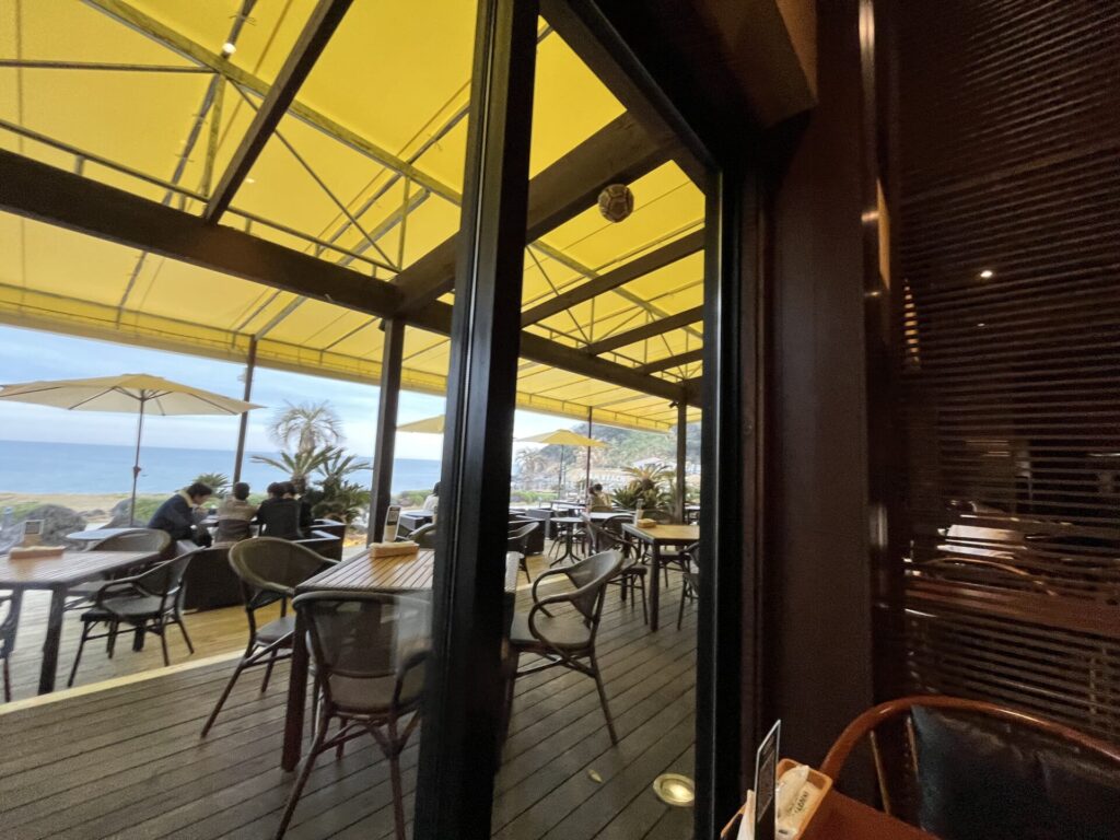 パームビーチレストランのテラス席。黄色いテントの深い庇が強い日差しを遮り、心地よい「あいまい空間」をつくる設計事例。