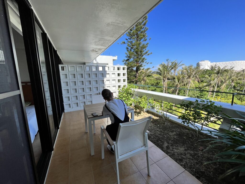 沖縄「ザ・ムーンビーチ ミュージアムリゾート」の客室テラス。深い庇の下に設えられたテーブルセットと、南国の青空が広がる開放的な景観。