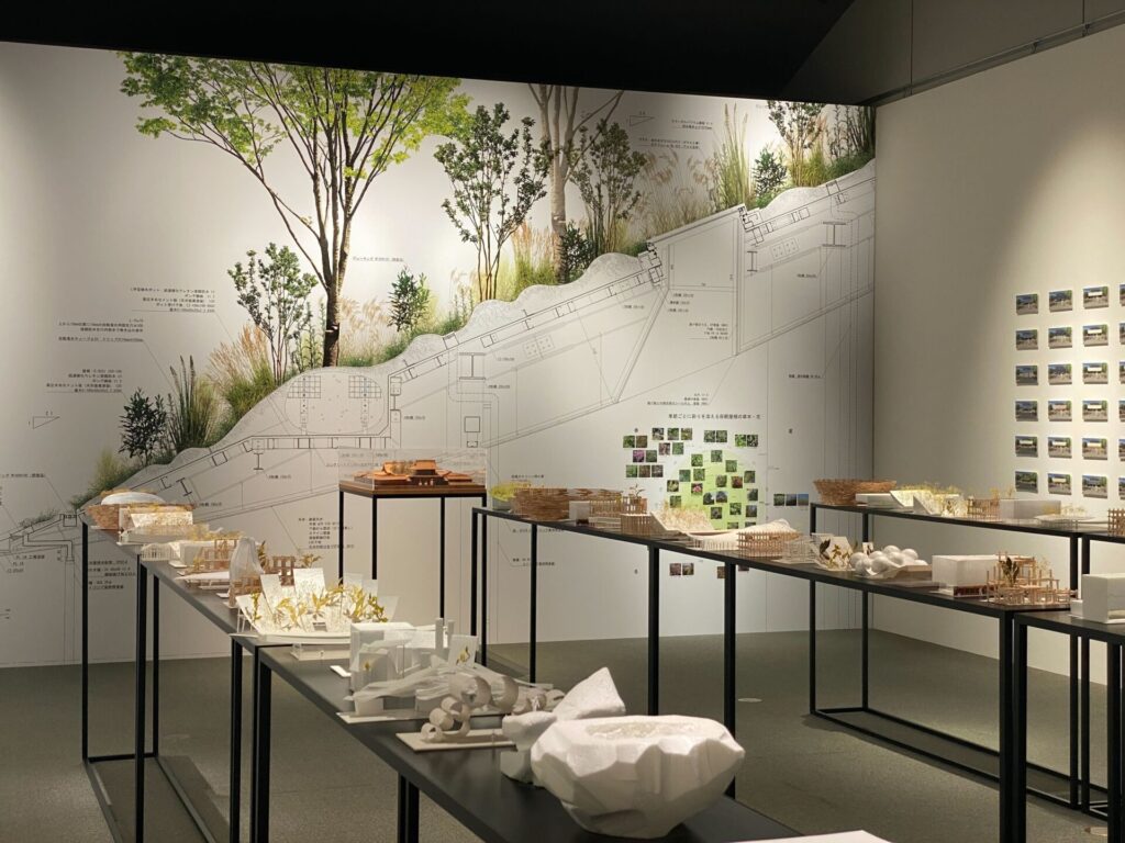 仮殿の断面図が描かれた巨大なパネルと、その前に並ぶスタディ模型。屋根の植栽や構造の仕組みを詳しく解説する展示コーナー。