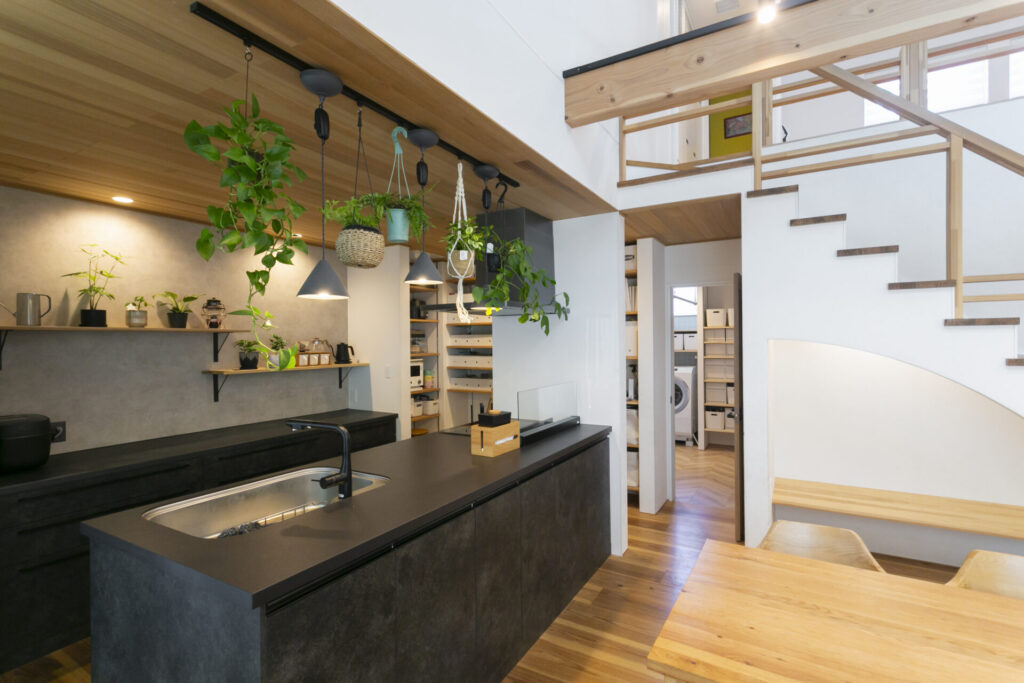 クリナップの最新システムキッチンを導入したLDK。吹き抜けとペンダントライト、吊り下げられた観葉植物が調和するカフェのような空間。