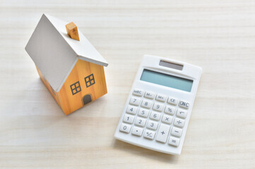 木製の家型模型と白い電卓。ZEH住宅の導入によるエネルギー収支と、将来の光熱費シミュレーションをイメージ。