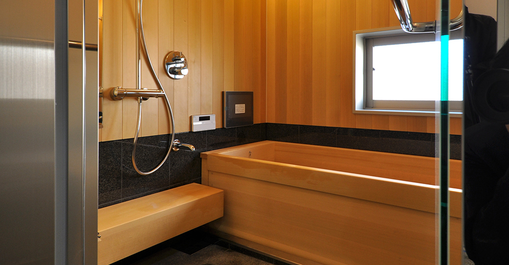 檜の壁板と浴槽で囲まれた温もりあるバスルーム。最新のシャワー設備と天然木の質感が融合した、癒しの入浴空間。