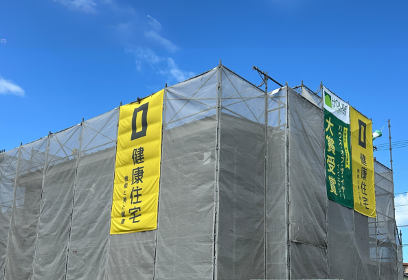青空の下、足場シートに囲まれた建築現場と「健康住宅」「大賞受賞」の懸垂幕