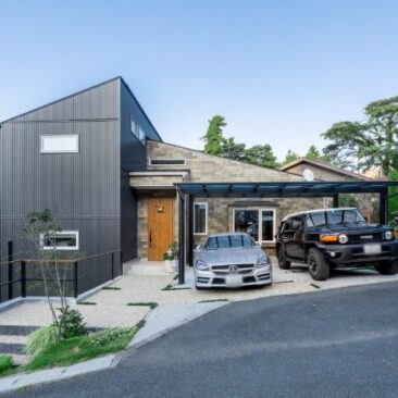 傾斜地に建つ、片流れ屋根とガレージが一体になった二階建て住宅の外観