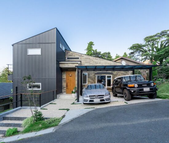 傾斜地に建つ、片流れ屋根とガレージが一体になった二階建て住宅の外観